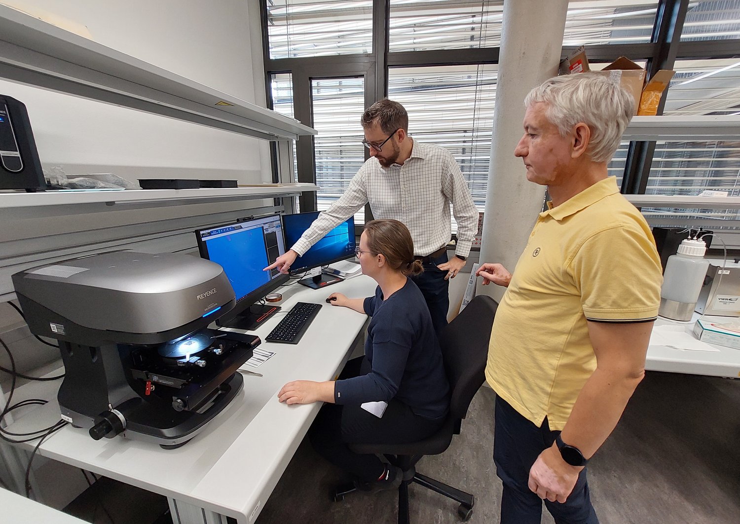 The three researchers in the lab, in front of the Keyence microscope. 