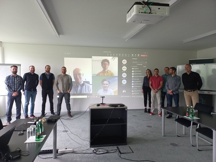 group picture at the kick-off, 9 people standing in front of a screen where you can see more people taking part online