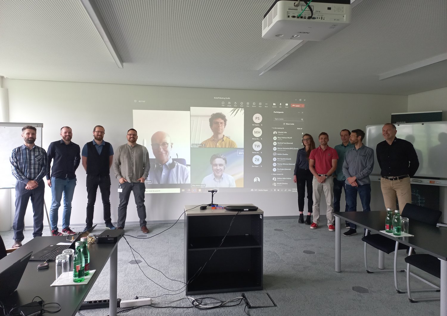 group picture at the kick-off, 9 people standing in front of a screen where you can see more people taking part online