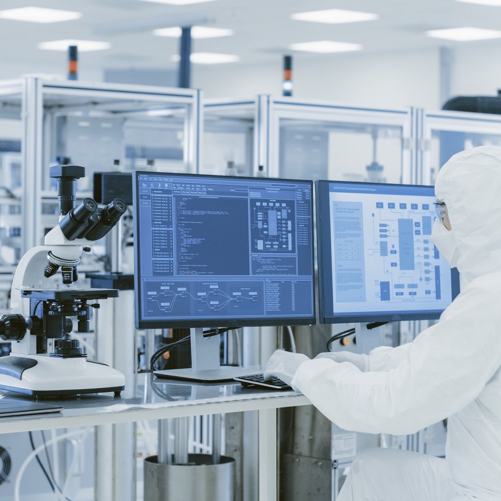 researcher in protective clothing standing next to a microscope in a lab