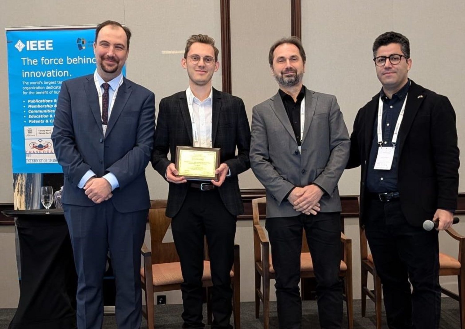 Four men in suits. In the middle is Alexander, holding the best paper award. Next to him Hans-Peter Bernhard, Head of Wireless Communications. To their left and right two people from the WF-IoT Conference. 