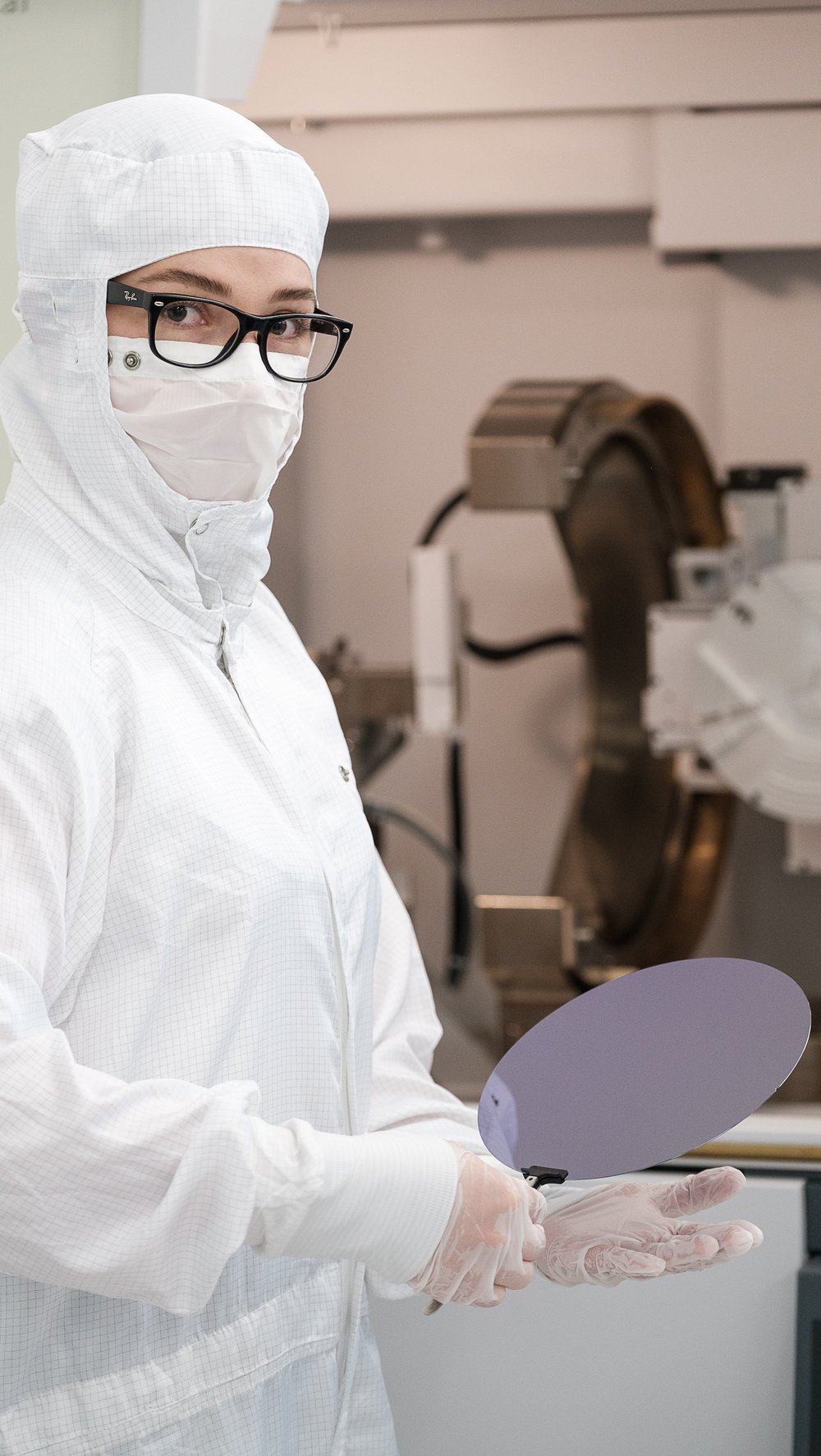 Madeleine in weißer Schutzausrüstung und Handschuhen im Reinraum. Sie hält einen Wafer in der Hand. 