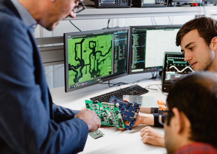 Three researchers with a printed circuit board in the lab