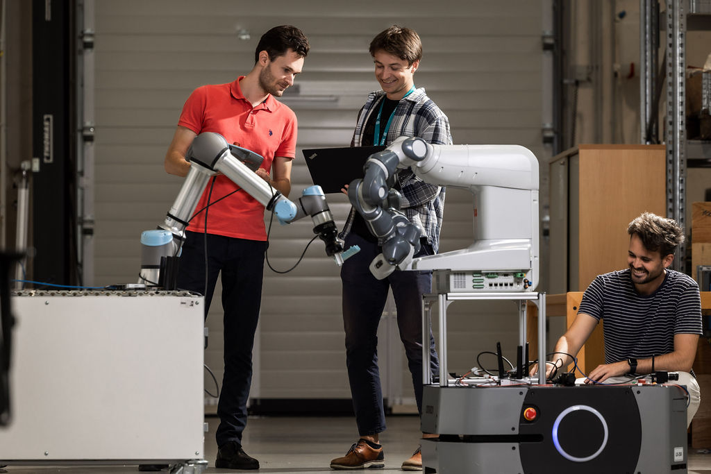 3 Forscher und ein Roboter in einer Industriehalle
